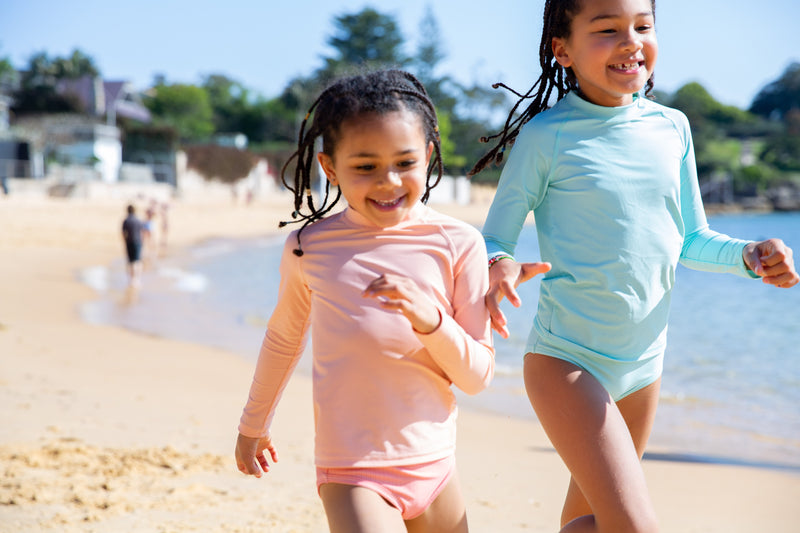 Girls Running On A Beach Wearing Peach And Green Colour Rash Guards With Long Sleeves 