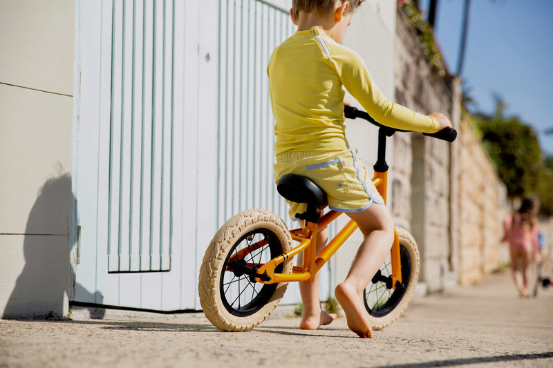 Boy On Bike Wearing Citrus Yellow Swim Shorts With Blue Detail Front 